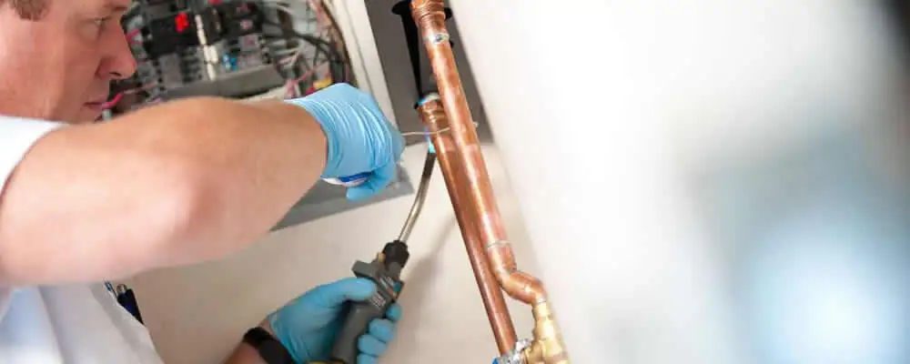 Water heater repair technician testing copper pipe connections and controls in Redding, CA
